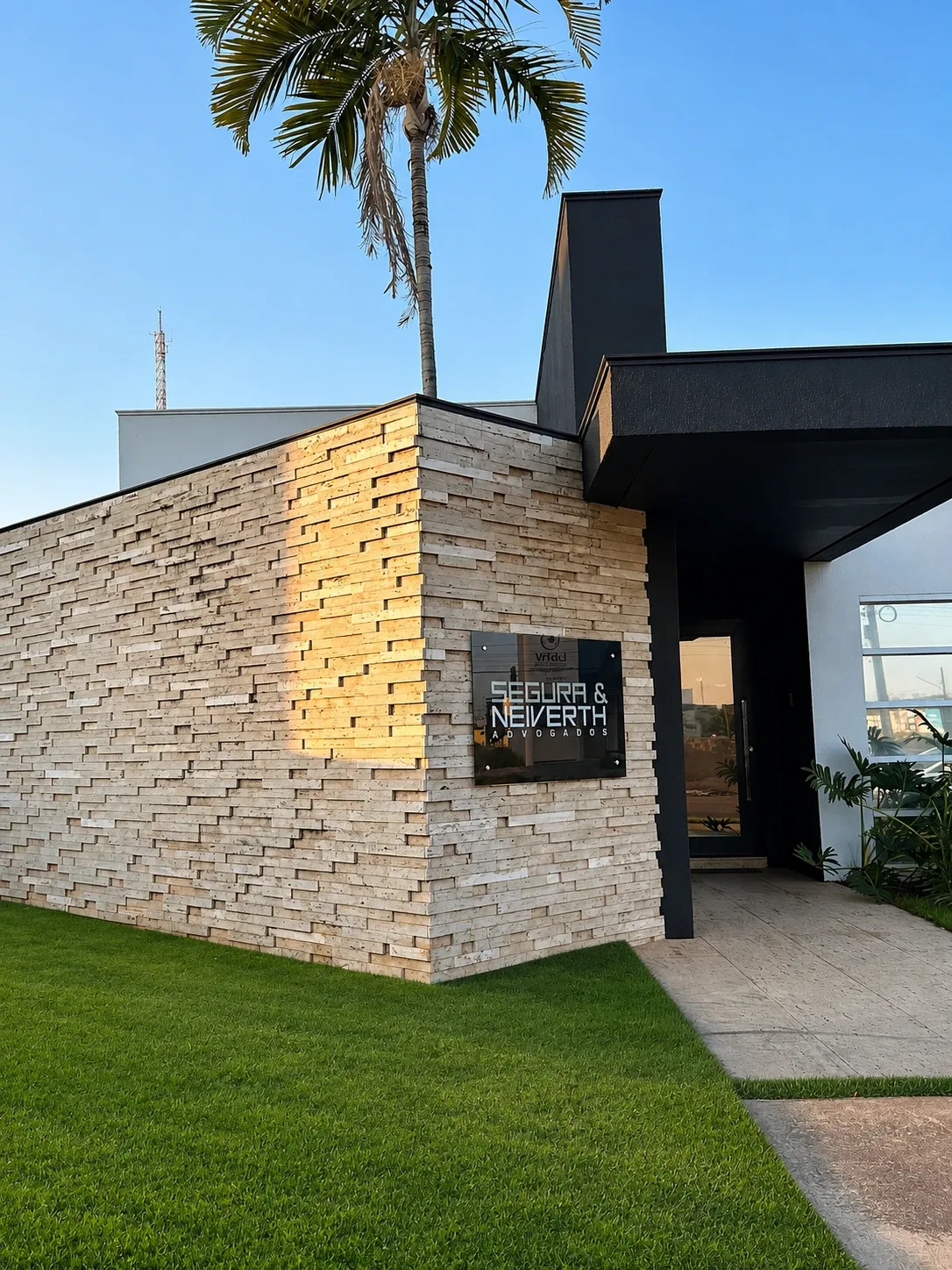 Quina de travertino do escritório recebendo a luz dourada do fim de tarde, com a placa do escritório.